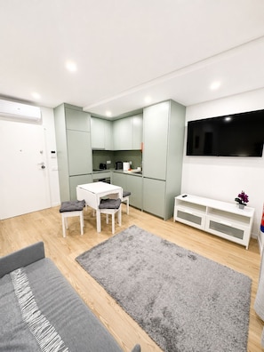 Una cocina moderna con comedor, un televisor de pantalla plana y una alfombra gris.