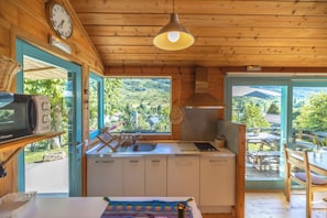 A wooden interior with a kitchen area, a dining table, and a view of the outdoors. - Cabañas Patagónicas (Maraña)
