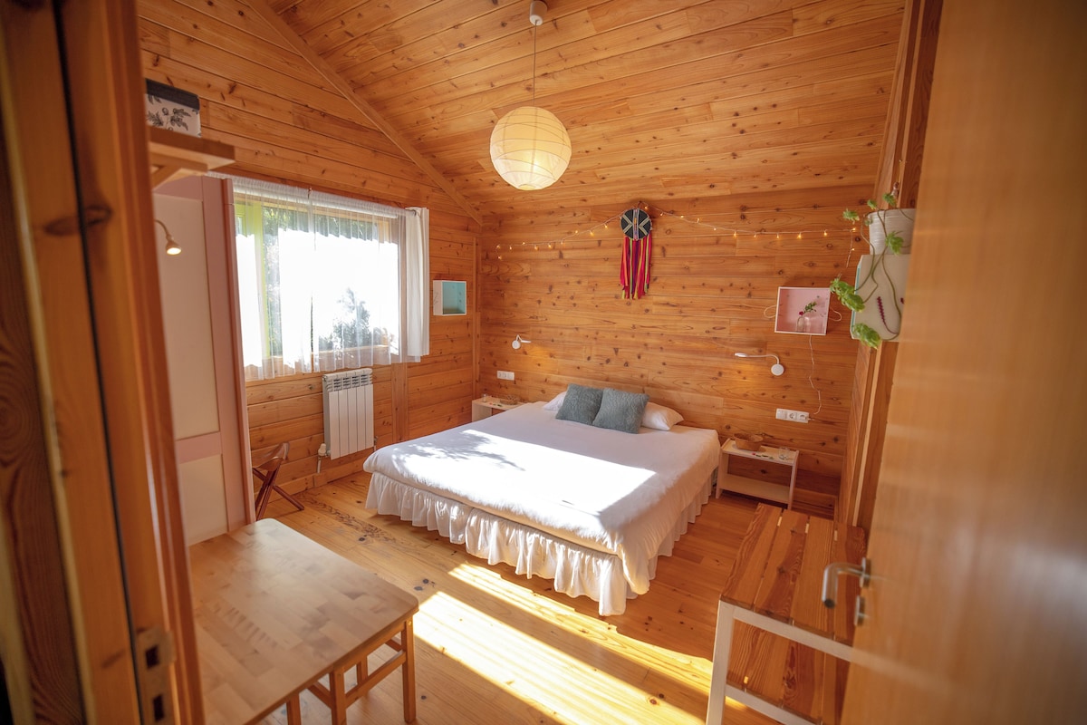 A wooden cabin bedroom with a bed, bedside table, and a window with curtains.