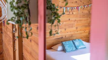 A wooden headboard with a string of colorful flags, a bed with white bedding and a blue pillow, and a plant in the foreground.