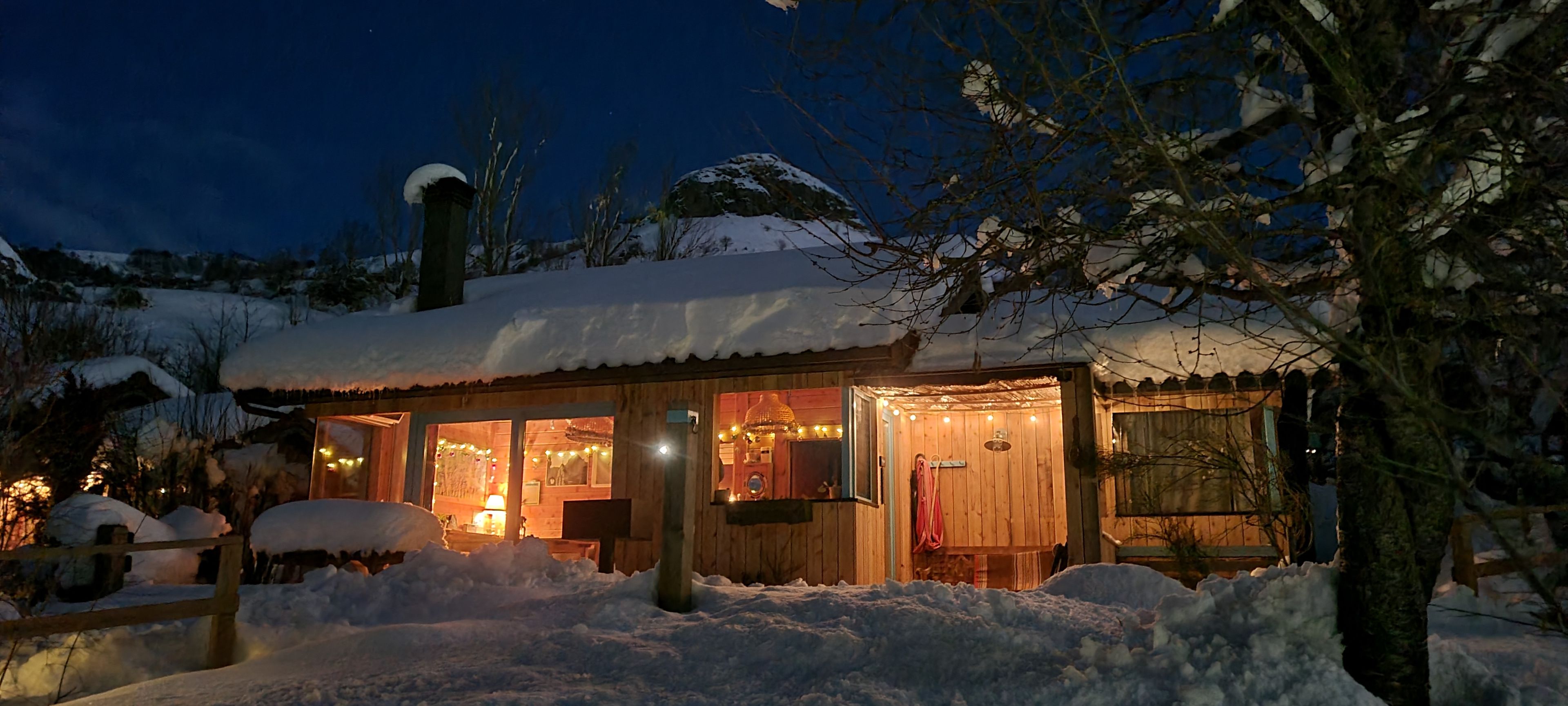 A wooden cabin with a snow-covered roof, illuminated windows, and a snow-covered landscape.