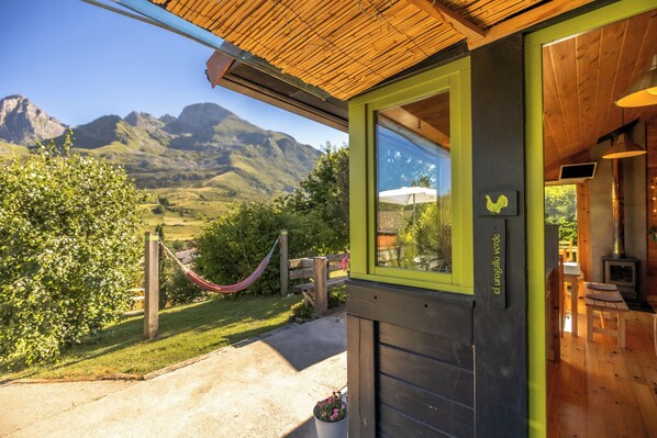 A wooden building with a green door and window, a hammock, and a view of mountains.