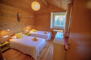 A wooden cabin room with two beds, a window with curtains, a hanging light fixture, and a small table.