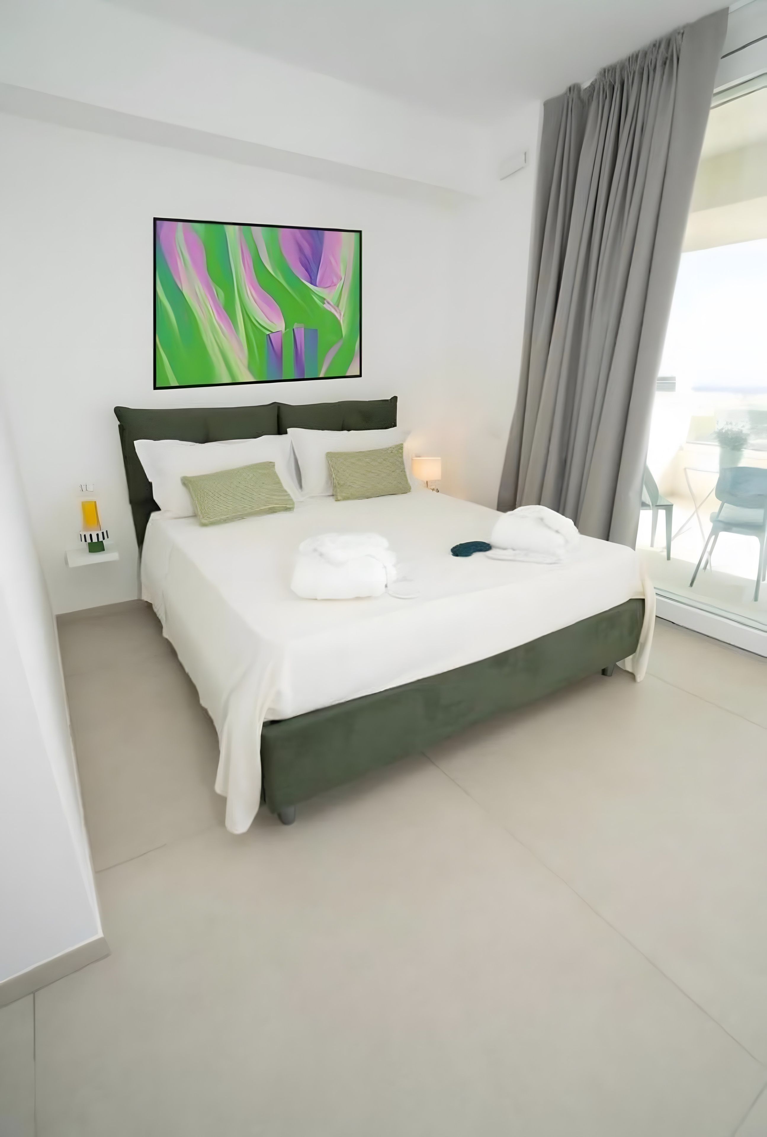 A modern hotel room with a large bed, a view of the outdoors, and a painting on the wall.