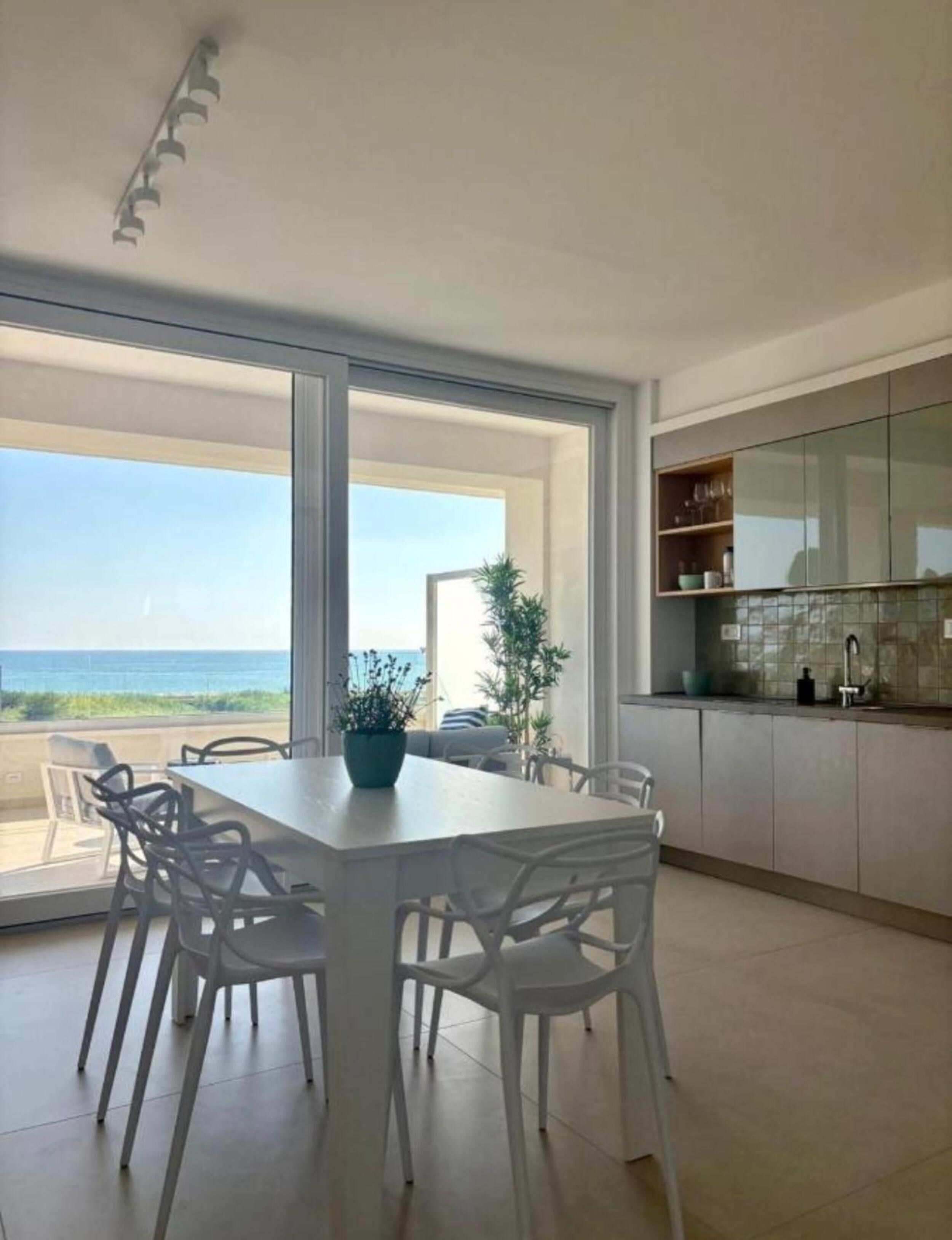A modern kitchen with a large window, a dining area with white chairs, and a view of the ocean.