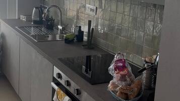 A modern kitchen with a stainless steel sink, a kettle, and a bread basket on the counter.