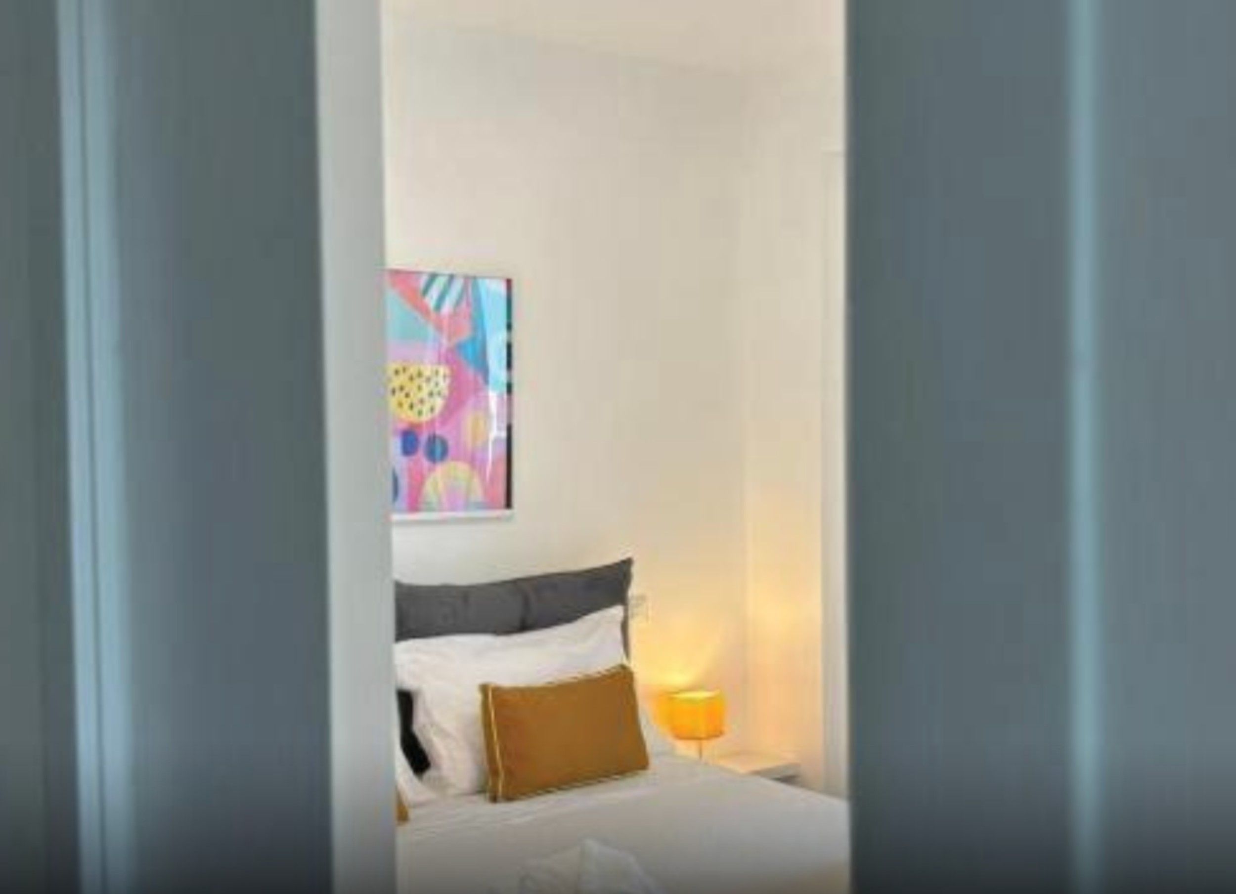 Una camera d'albergo con un letto, una lampada da comodino e un quadro astratto dai colori vivaci appeso al muro.