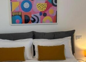 Ein Bett mit Kopfteil, zwei Kissen und einem farbenfrohen, abstrakten Gemälde an der Wand.