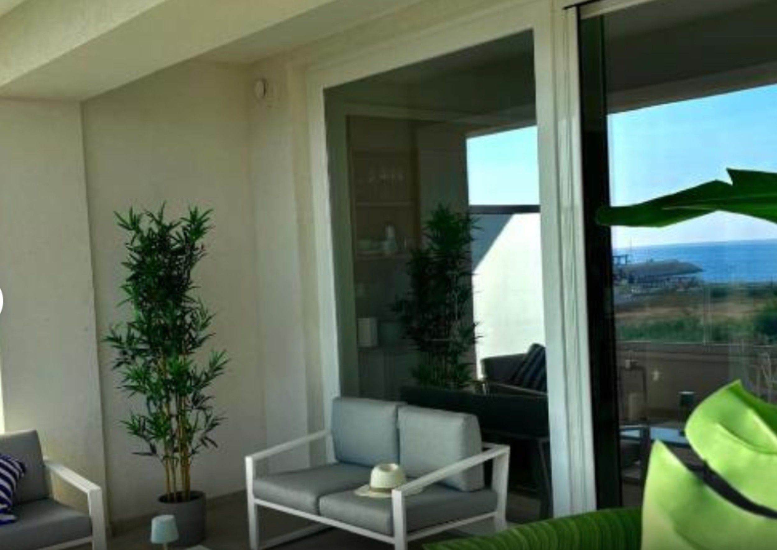 A balcony with a sofa, a chair, and two potted plants.