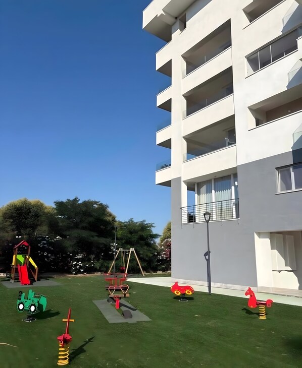 Un’area giochi con diverse strutture ricreative, un prato verde e un edificio moderno con balconi.