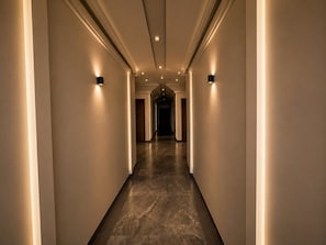 A corridor with walls on either side, recessed lighting, and a marble floor.