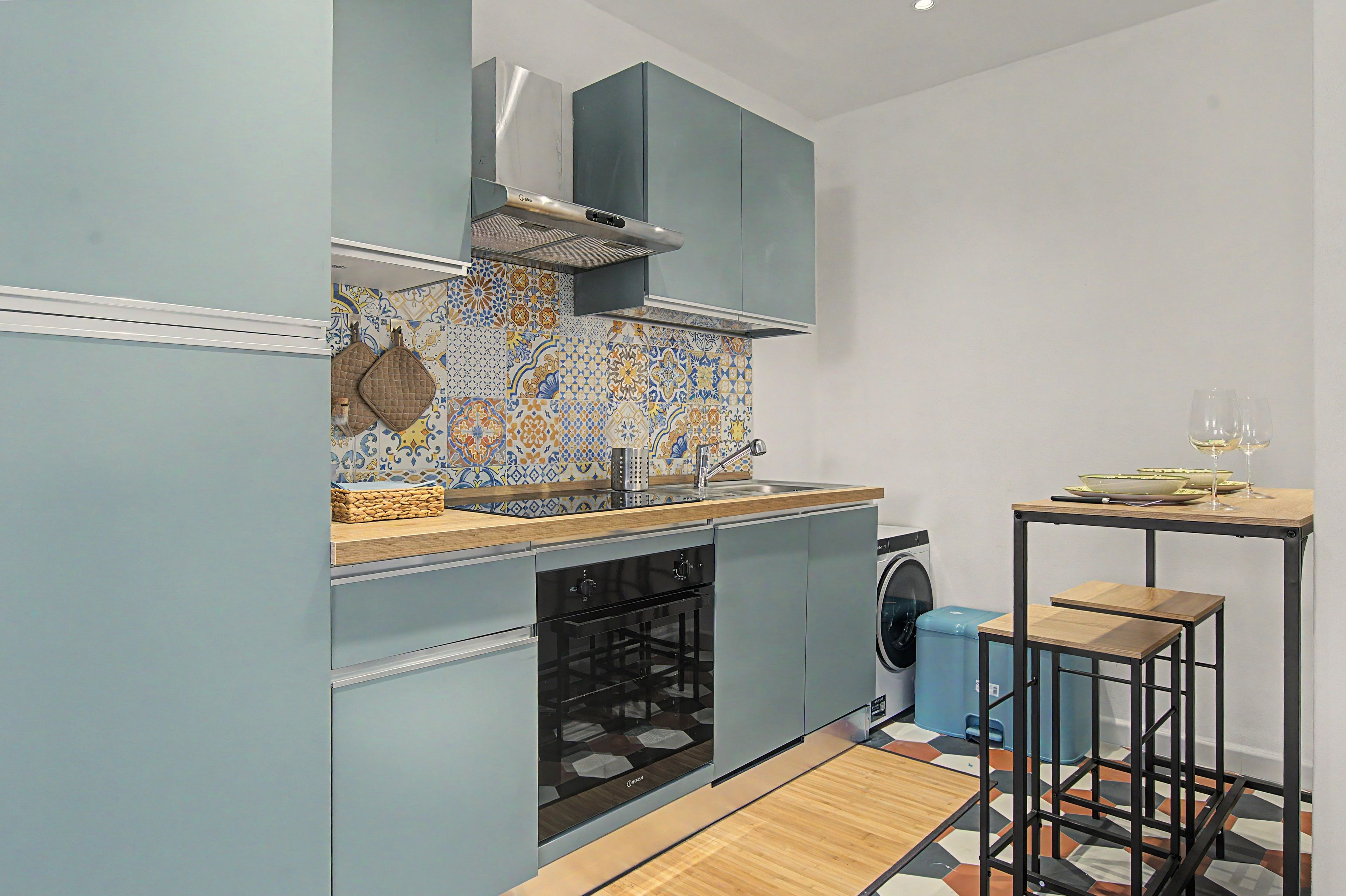 A compact kitchen with a washing machine, a sink, and a small dining area with stools.