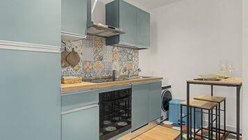A compact kitchen with a washing machine, a sink, and a small dining area with stools.