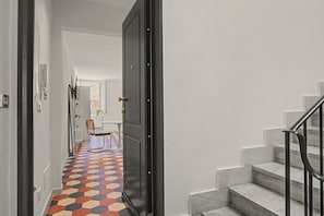 Passadís amb un paviment de disseny geomètric, una cadira, un escriptori i una escala amb barana.