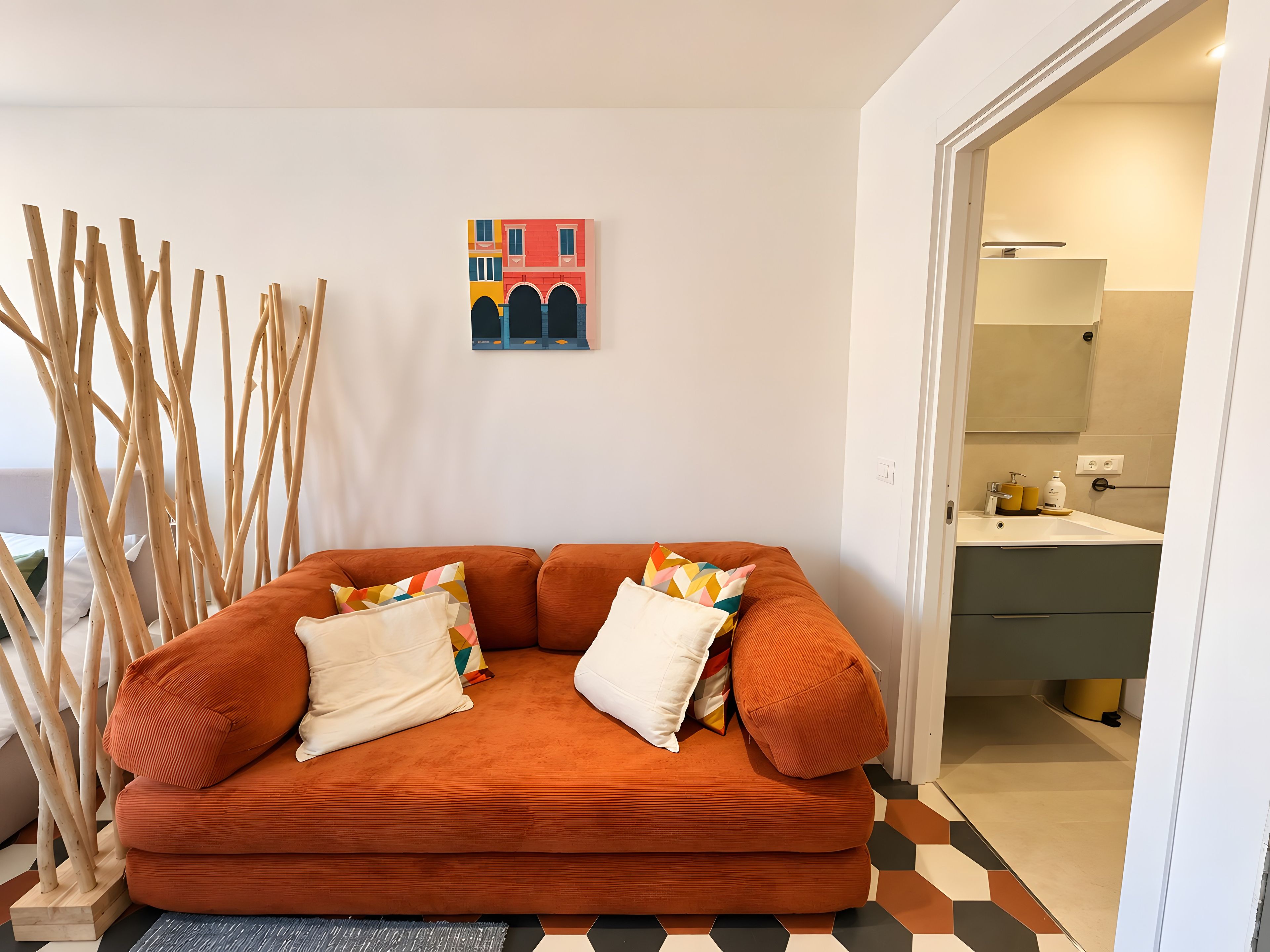 A room with a sofa, a colorful abstract painting, and a view into a bathroom.