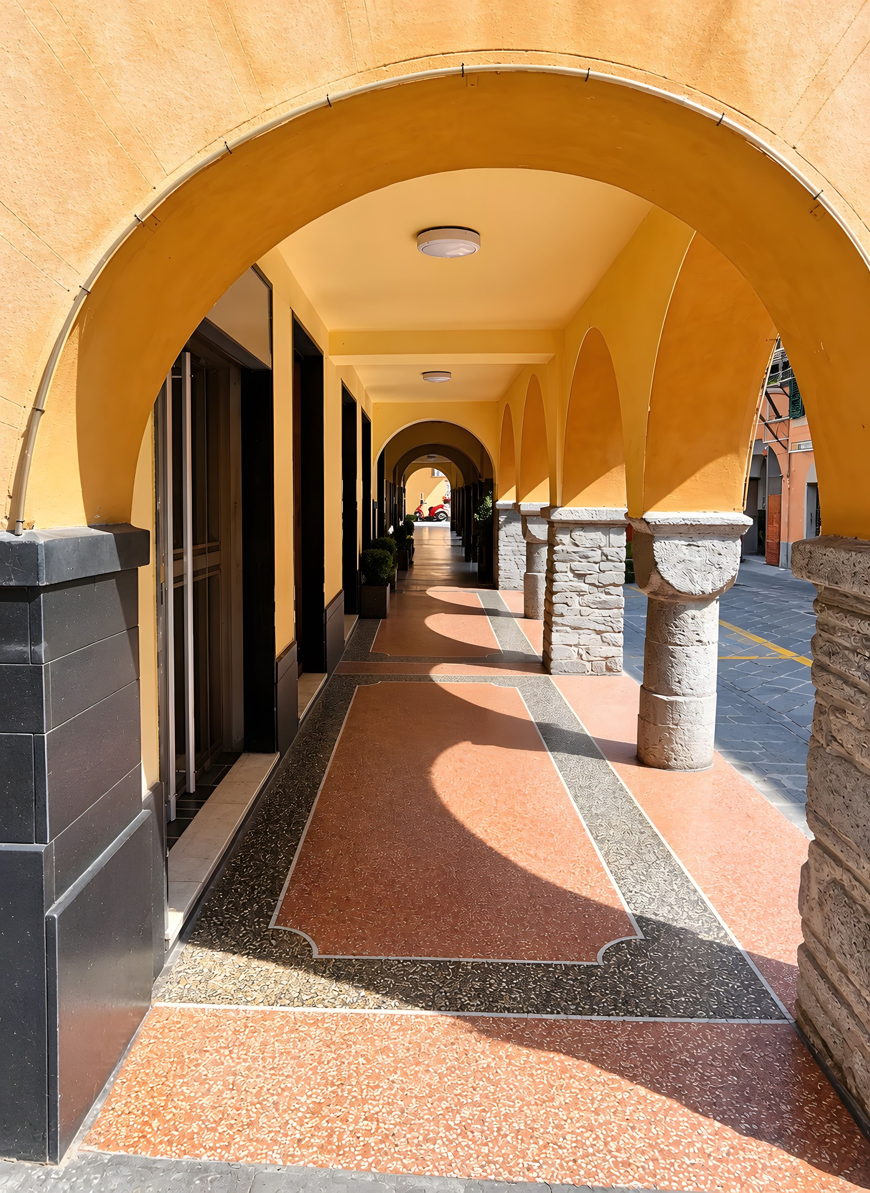 A corridor with arches, a tiled floor, and a scooter parked in the distance.