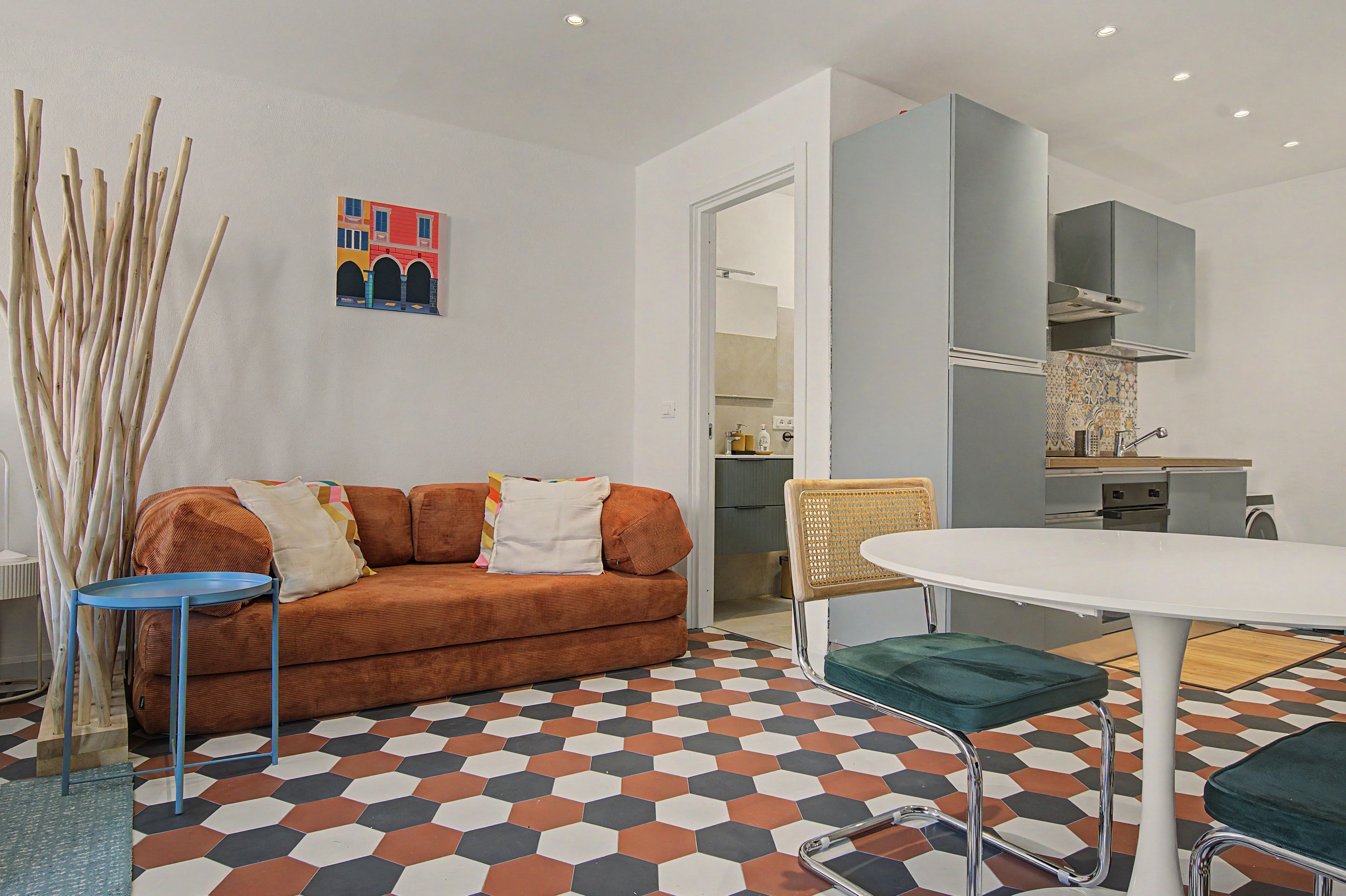 A modern living room with a sofa, a dining table, and a kitchen in the background.