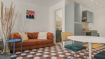 A modern living room with a sofa, a dining table, and a kitchen in the background.