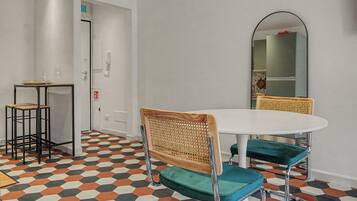 A dining area with a round table, two chairs, a small side table, and a mirror on the wall.
