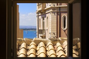 A view of a building with a tiled roof and a balcony overlooking a body of water with boats. - Dimora Italia Blu Calypso Ortigia (Ortigia)
