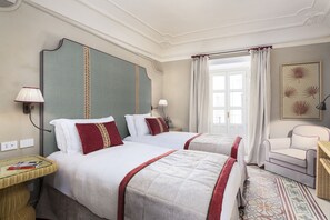 Een hotelkamer met twee bedden, een zithoek met een fauteuil, een tafeltje en een raam met gordijnen.