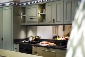 A kitchen with light green cabinets, a black countertop, and various kitchen items including pots, a bread loaf, and a bowl of grapes. - Dimora Italia Bianca Arethusa Ortigia (Ortigia)