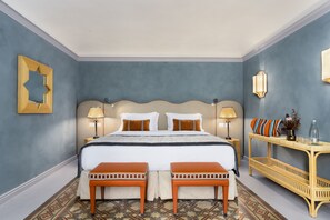 Habitación de hotel con una cama grande, dos mesitas de noche, una pequeña mesa con adornos y un suelo estampado.