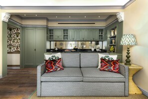 Un espacio de sala acogedor con un sofá estampado, una cocina con armarios verdes y una pared decorativa.