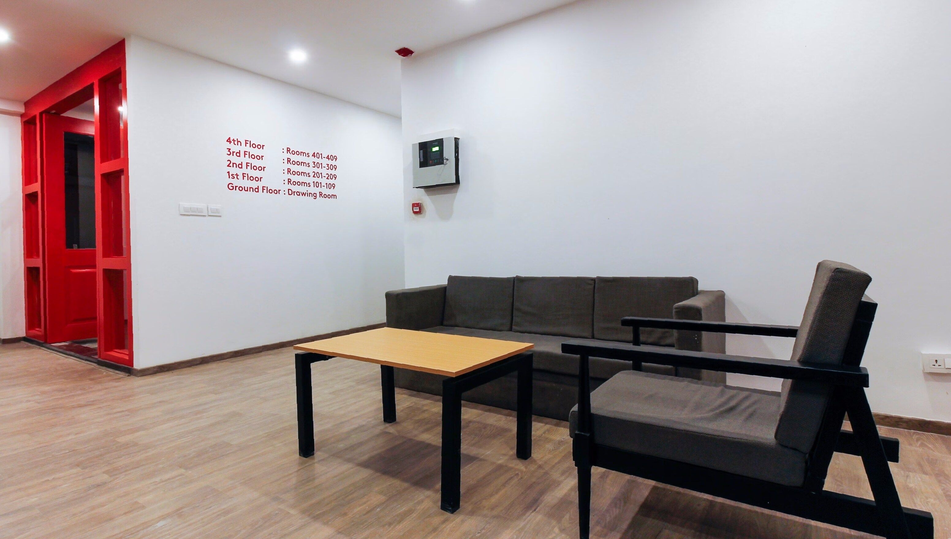 Um interior moderno com uma porta vermelha, um sofá, uma mesa e um dispositivo fixado na parede.