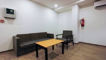 Quarto com sofá, poltrona, mesa pequena, extintor de incêndio e termostato na parede.