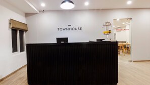 A reception desk with a sign reading 'OYO TOWNHOUSE' in a modern interior with a dining area visible in the background. - Super Townhouse RCC Elite (Hyderabad)