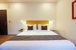 Una habitación de hotel con cama, mesitas de noche, teléfono y puerta.