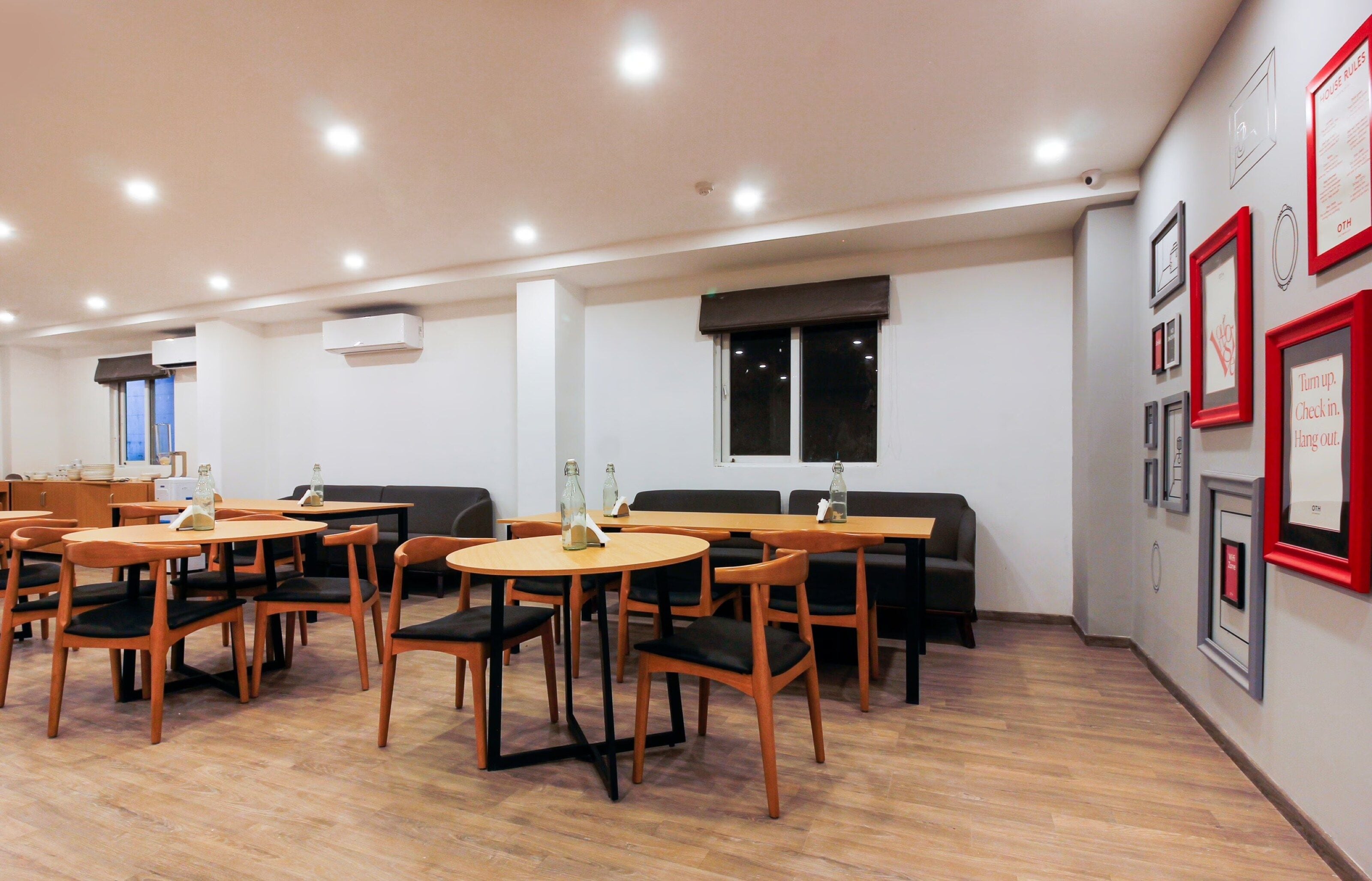 Un comedor moderno con mesas y sillas redondas, un sofá negro, y una pared decorada con cuadros y letreros.