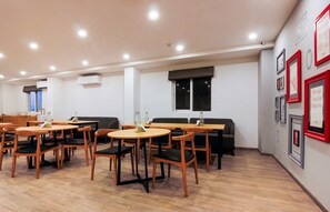 Un comedor moderno con mesas y sillas redondas, un sofá negro, y una pared decorada con cuadros y letreros.