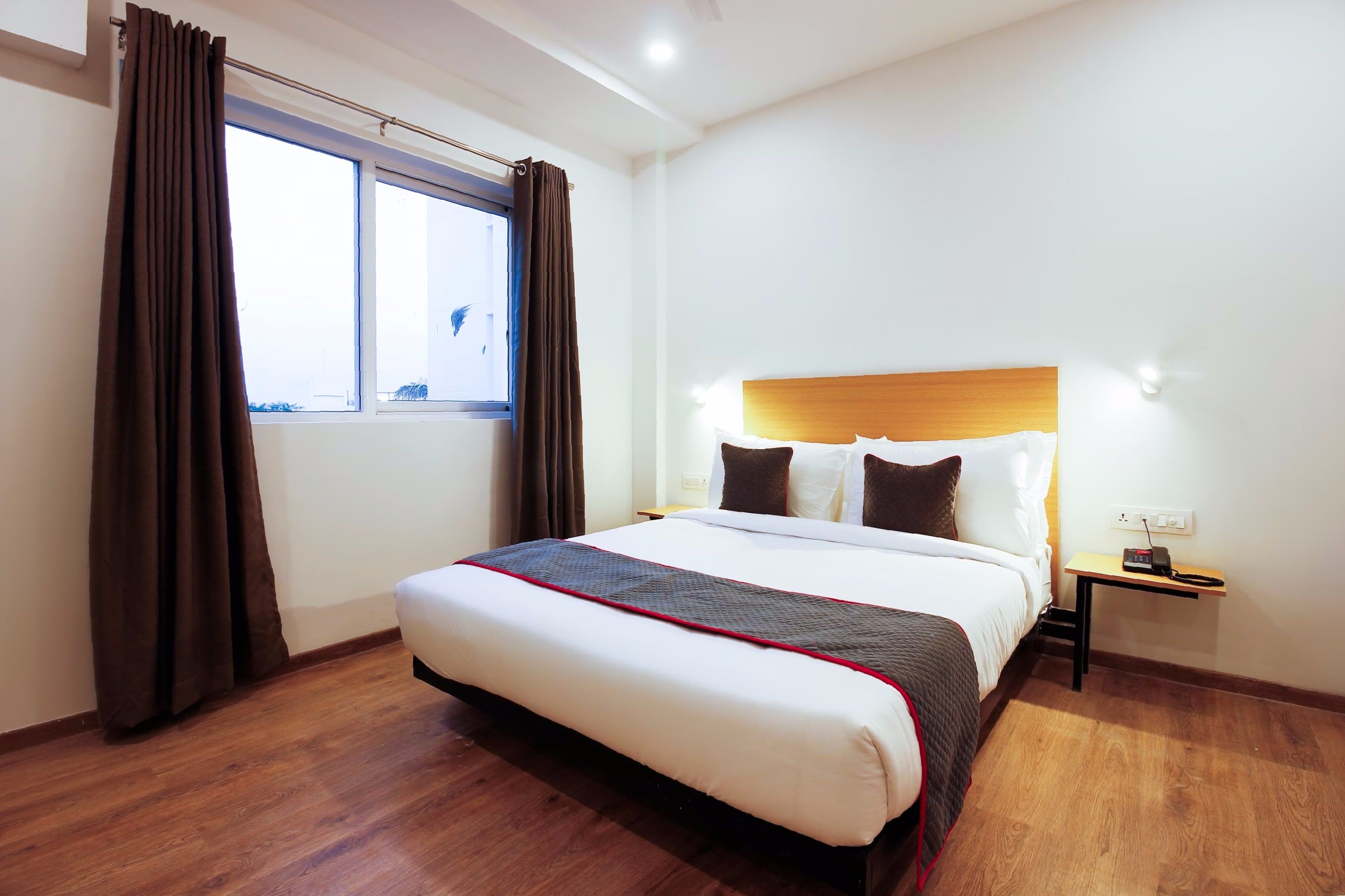 Une chambre d’hôtel avec un grand lit, une table de chevet, une fenêtre avec des rideaux et un plancher en bois.