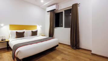 Una habitación de hotel con una cama, mesita de noche, lámpara y un equipo de aire acondicionado.