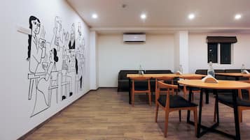 A dining area with wooden tables and chairs, a wall mural, and an air conditioning unit.