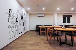 Un comedor con mesas y sillas de madera, un mural en la pared y un equipo de aire acondicionado.