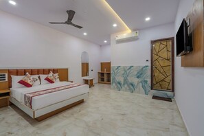 A bedroom with a bed, a ceiling fan, an air conditioning unit, and a television mounted on the wall.