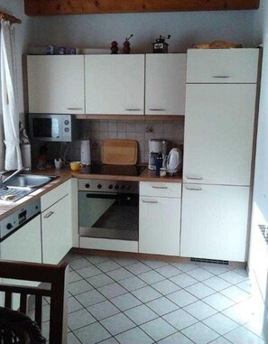 A compact kitchen with white cabinets, a microwave, a toaster, and a refrigerator. - Hafenmöwe Vacation Home - Carolinensiel (Wittmund)