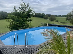 Ein Schwimmbecken mit Holzterrasse, umgeben von Grünpflanzen und Bäumen.