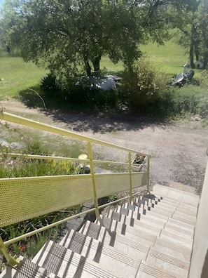 Eine Treppe führt zu einem überdachten Außenbereich mit Metallgeländer und Blick auf ein grünes Feld.