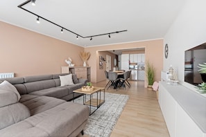 A modern living room with a grey sectional sofa, a small wooden coffee table, and a dining area with a round table and chairs. - Sea-view Stay With Garage (Blankenberge)