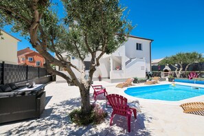 A poolside area with lounge chairs, a small tree, and a building in the background. - Villa Feliks Zadarvillas (Razanac)