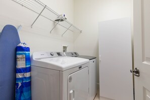 Een wasserette met een witte wasmachine en droger, een metalen droogrek, en een blauw gestreept voorwerp aan de muur.