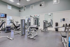 Een sportschool met diverse fitnessapparaten, een televisie en een spiegel.