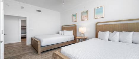 A hotel room with two beds, a wooden floor, a ceiling fan, and a door leading to a bathroom.