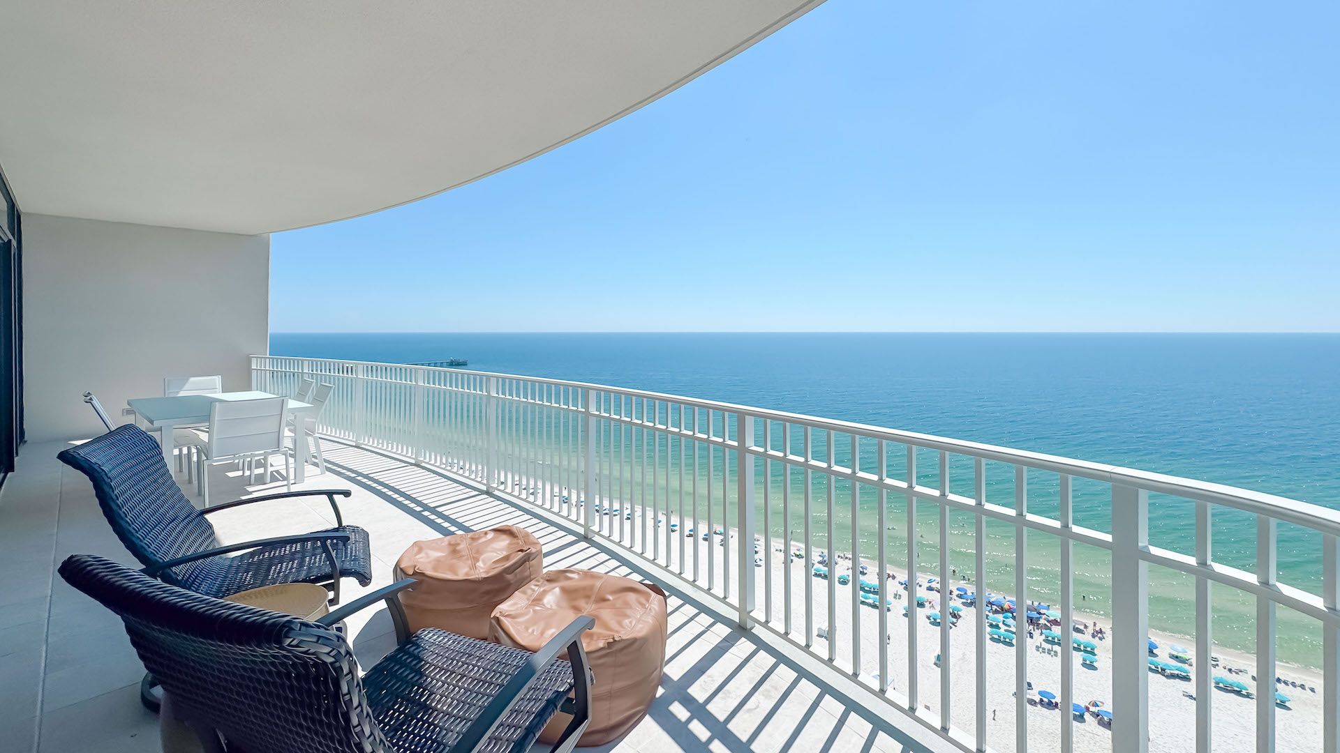 A balcony with a view of the ocean, white railings, and outdoor furniture.