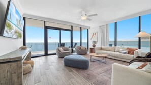 A spacious living room with a balcony overlooking the sea, featuring a ceiling fan, a sofa, armchairs, and a coffee table. - Unreal Views from this Beachfront 4BR Beauty! (Gulf Shores)