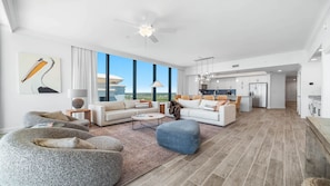 A modern living room with a large window, a ceiling fan, and a view of a building. - Unreal Views from this Beachfront 4BR Beauty! (Gulf Shores)